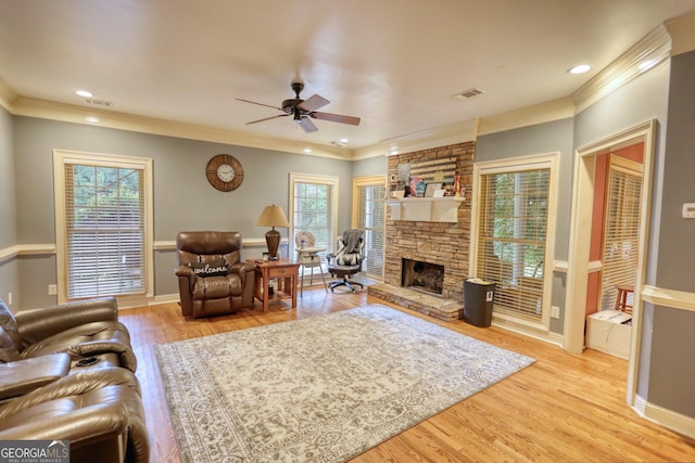 living room with a stone fireplace, ceiling fan, crown molding, and light wood-type flooring