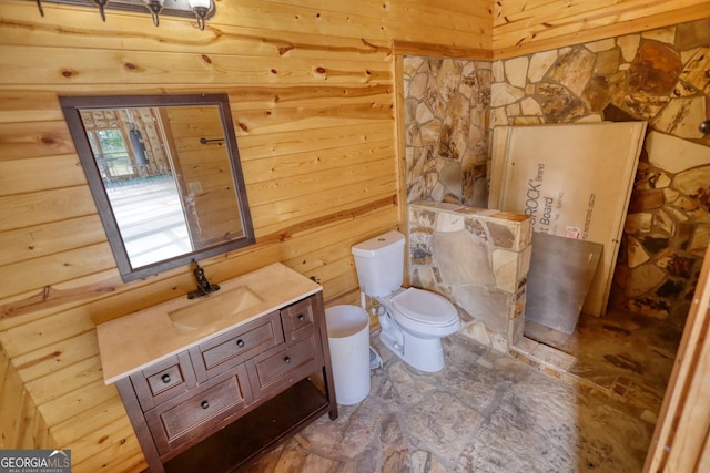 bathroom with vanity, toilet, and wood walls