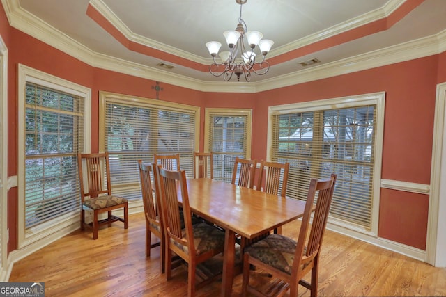 dining space featuring a chandelier, light wood-type flooring, ornamental molding, and a tray ceiling