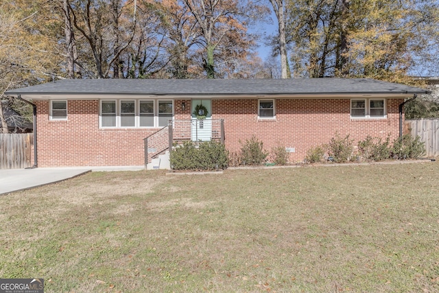 ranch-style house with a front lawn, a shingled roof, fence, and brick siding