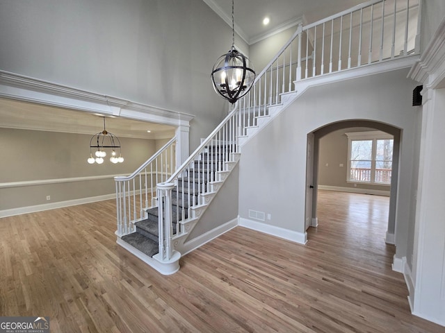 stairs with hardwood / wood-style floors, a towering ceiling, ornamental molding, and a notable chandelier