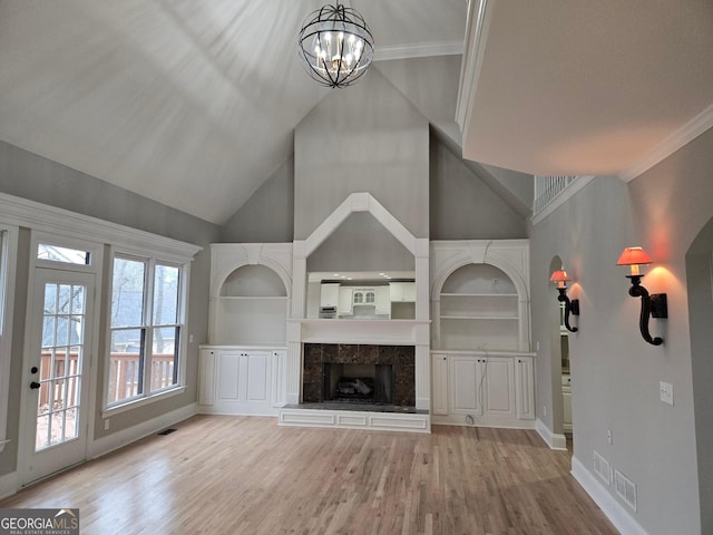 unfurnished living room featuring crown molding, a premium fireplace, a towering ceiling, a notable chandelier, and light hardwood / wood-style floors