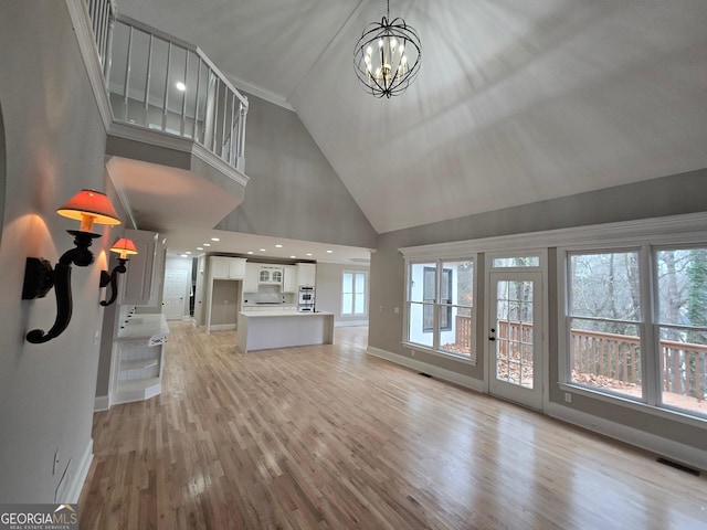 unfurnished living room with a notable chandelier, light wood-type flooring, and high vaulted ceiling