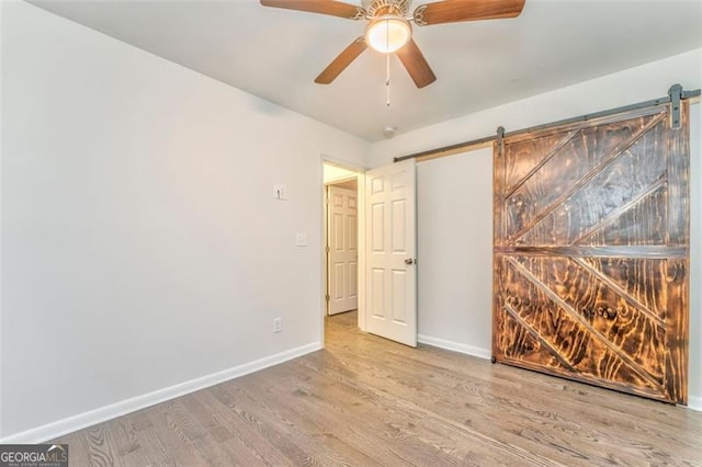 spare room featuring ceiling fan, a barn door, and light hardwood / wood-style floors