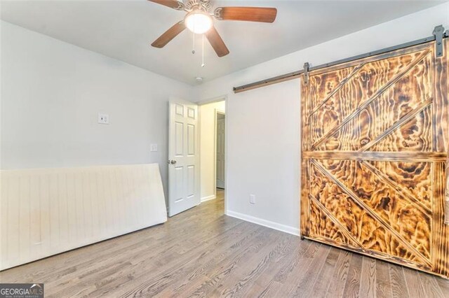 spare room featuring a barn door, ceiling fan, and hardwood / wood-style flooring