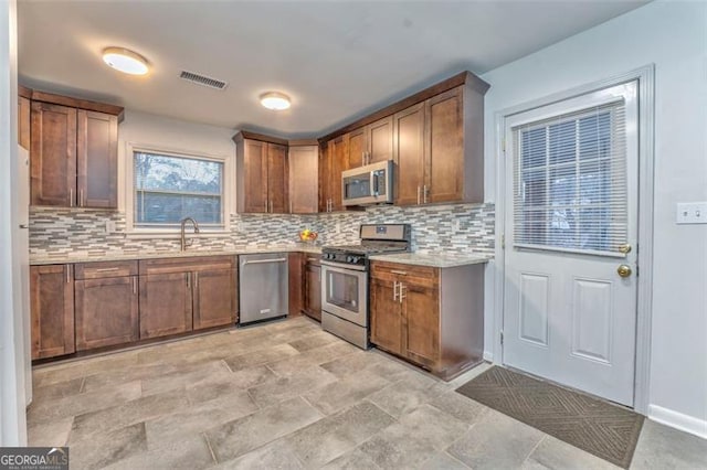 kitchen with decorative backsplash, light stone countertops, sink, and appliances with stainless steel finishes