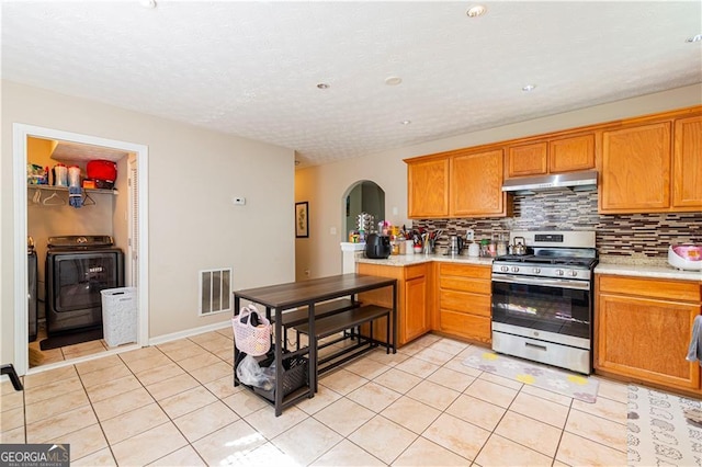 kitchen featuring gas stove, washing machine and dryer, backsplash, kitchen peninsula, and light tile patterned floors