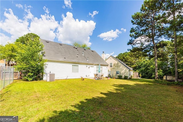 rear view of house featuring central AC unit and a lawn