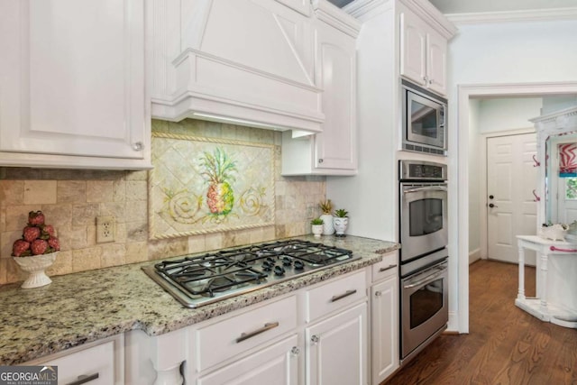 kitchen featuring decorative backsplash, stainless steel appliances, white cabinetry, and premium range hood