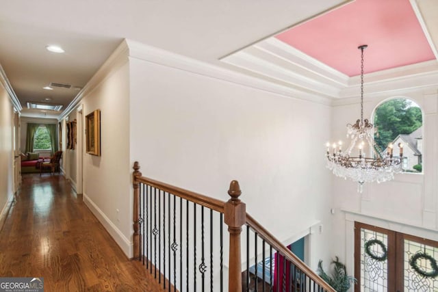 hall featuring a notable chandelier, a raised ceiling, crown molding, and dark wood-type flooring