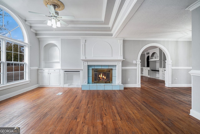 unfurnished living room with ceiling fan, built in features, a textured ceiling, a fireplace, and ornamental molding