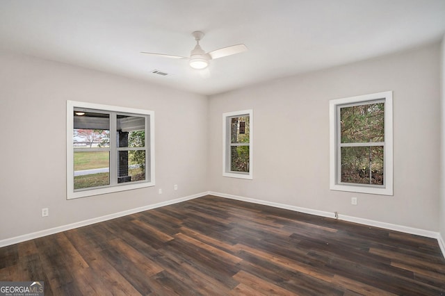 empty room featuring a wealth of natural light, ceiling fan, and dark wood-type flooring