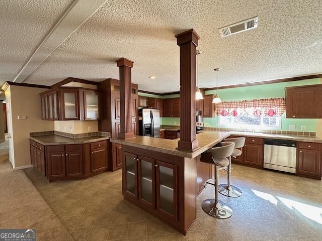 kitchen featuring a center island, ornamental molding, a kitchen bar, stainless steel appliances, and decorative columns