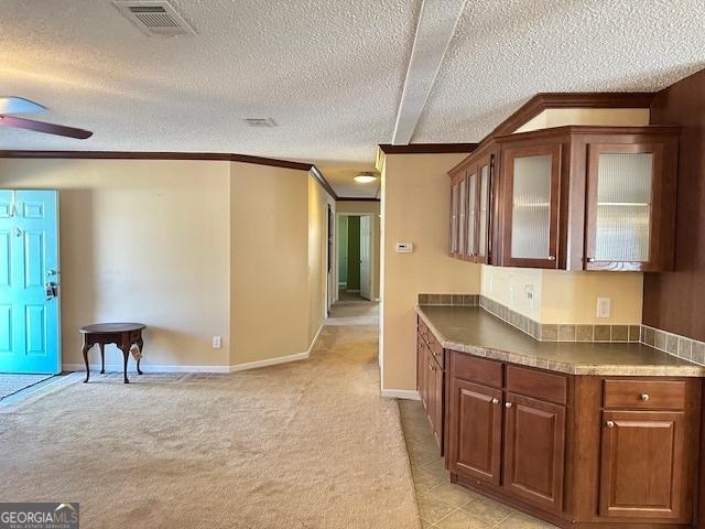 kitchen featuring a textured ceiling, light colored carpet, ceiling fan, and ornamental molding