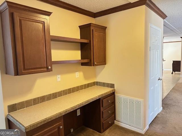 unfurnished office with dark colored carpet, built in desk, ornamental molding, and a textured ceiling