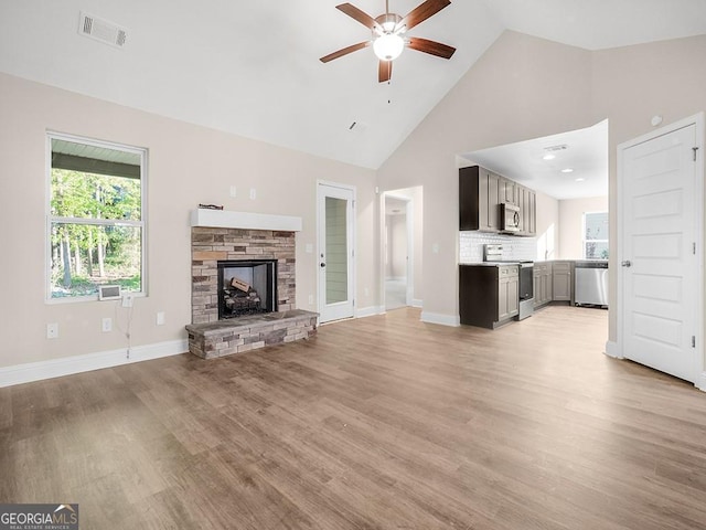 unfurnished living room featuring ceiling fan, light hardwood / wood-style floors, a stone fireplace, and high vaulted ceiling