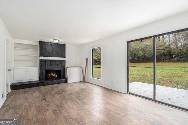 unfurnished living room with hardwood / wood-style flooring, a stone fireplace, and built in features