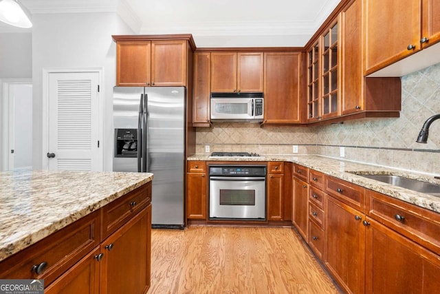 kitchen with light stone countertops, backsplash, stainless steel appliances, sink, and light hardwood / wood-style flooring