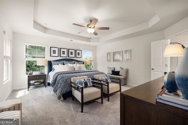 bedroom with a raised ceiling, ceiling fan, and light carpet