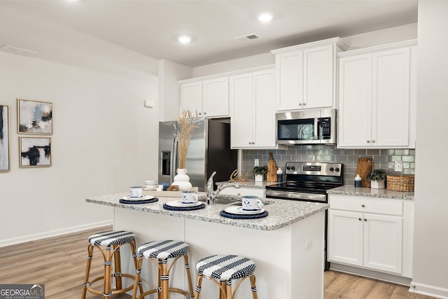 kitchen featuring tasteful backsplash, white cabinetry, a center island with sink, and stainless steel appliances