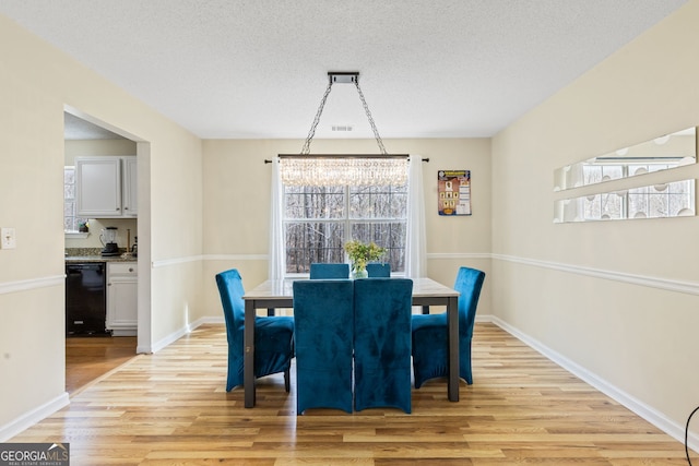 dining space with light wood-style flooring, visible vents, baseboards, and a textured ceiling