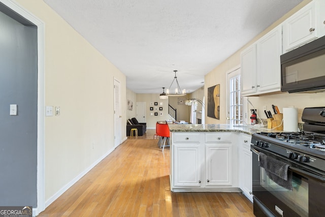 kitchen with light wood-style floors, a peninsula, an inviting chandelier, black appliances, and white cabinetry