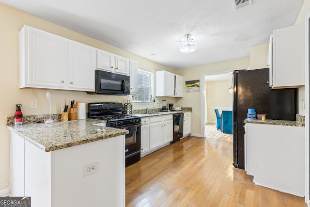 kitchen with visible vents, light wood-style floors, white cabinetry, a peninsula, and black appliances