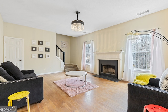 living room with light wood finished floors, visible vents, a fireplace with raised hearth, baseboards, and stairs