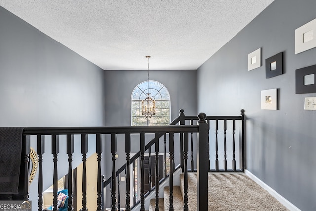 hallway featuring a textured ceiling, carpet flooring, an upstairs landing, baseboards, and an inviting chandelier