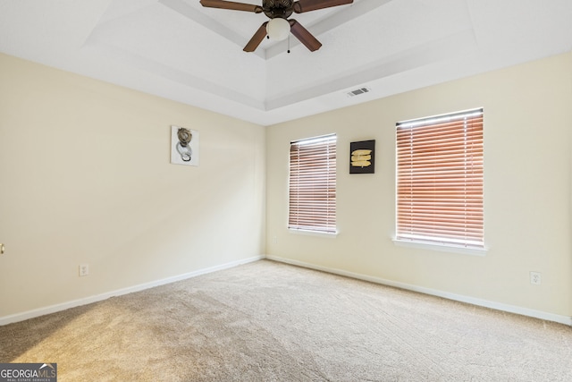 carpeted empty room featuring visible vents, a tray ceiling, ceiling fan, and baseboards