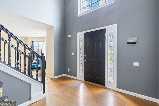 entryway featuring a towering ceiling, hardwood / wood-style flooring, stairs, and baseboards