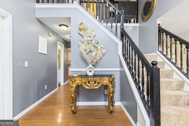 stairs featuring a towering ceiling, baseboards, and wood finished floors