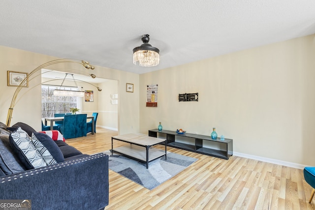 living area with an inviting chandelier, a textured ceiling, baseboards, and wood finished floors