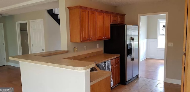 kitchen featuring a textured ceiling, light tile patterned flooring, kitchen peninsula, and stainless steel refrigerator with ice dispenser