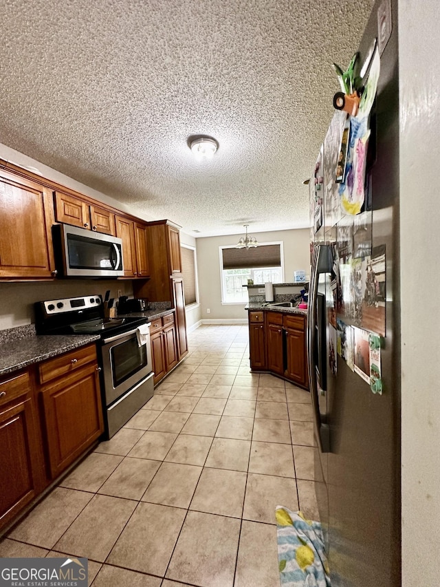 kitchen featuring stainless steel appliances, decorative light fixtures, light tile patterned flooring, dark stone countertops, and a notable chandelier