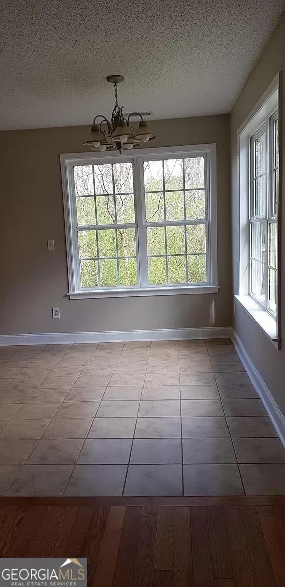 unfurnished dining area with a textured ceiling, an inviting chandelier, and light tile patterned floors