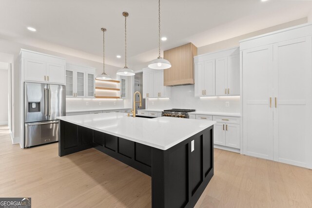 kitchen featuring white cabinetry, sink, high quality fridge, a kitchen island with sink, and range