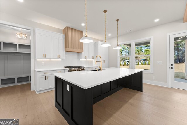 kitchen featuring white cabinets, a center island with sink, sink, hanging light fixtures, and range