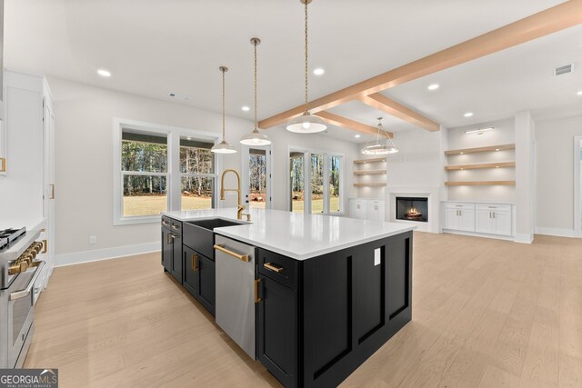 kitchen with pendant lighting, a center island with sink, sink, beamed ceiling, and stainless steel appliances