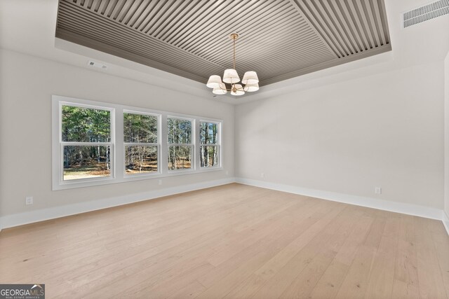 unfurnished room featuring a raised ceiling, light wood-type flooring, and an inviting chandelier