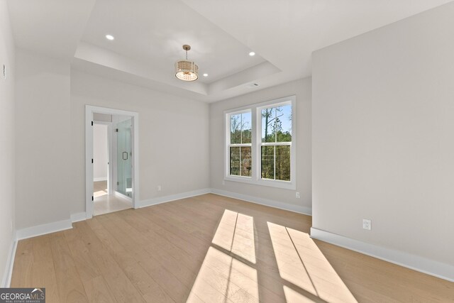 unfurnished room featuring a raised ceiling, light hardwood / wood-style flooring, and an inviting chandelier