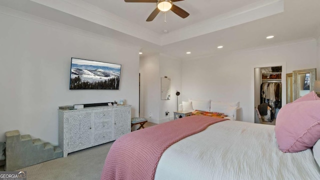 carpeted bedroom with a raised ceiling, a walk in closet, crown molding, ceiling fan, and a closet