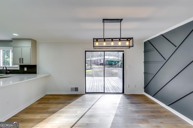 unfurnished dining area with light hardwood / wood-style floors, ornamental molding, and sink