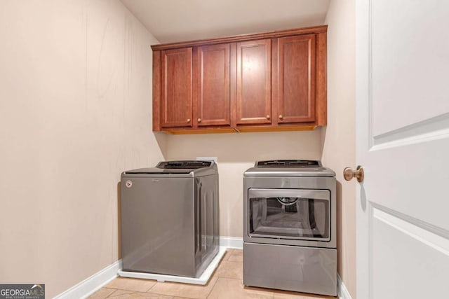 clothes washing area with cabinets, light tile patterned floors, and washing machine and clothes dryer