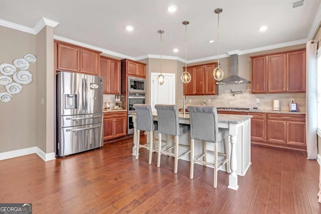 kitchen featuring appliances with stainless steel finishes, light stone counters, wall chimney range hood, pendant lighting, and an island with sink