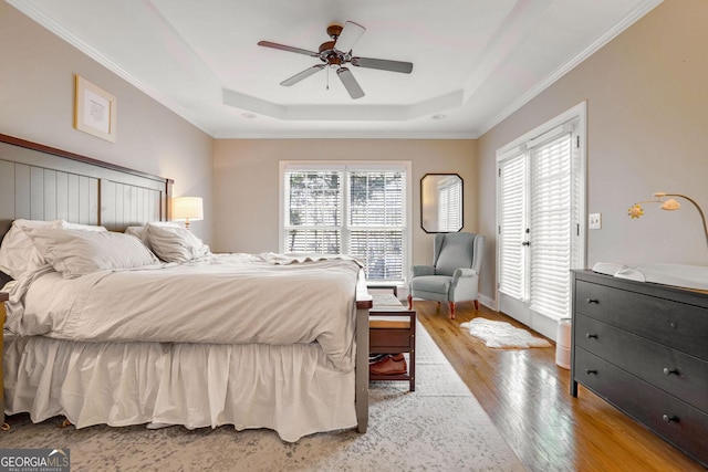 bedroom featuring ceiling fan, light hardwood / wood-style floors, multiple windows, and a tray ceiling