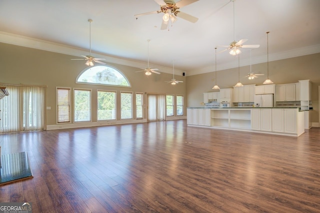 unfurnished living room featuring dark wood-type flooring, a towering ceiling, a healthy amount of sunlight, and ornamental molding