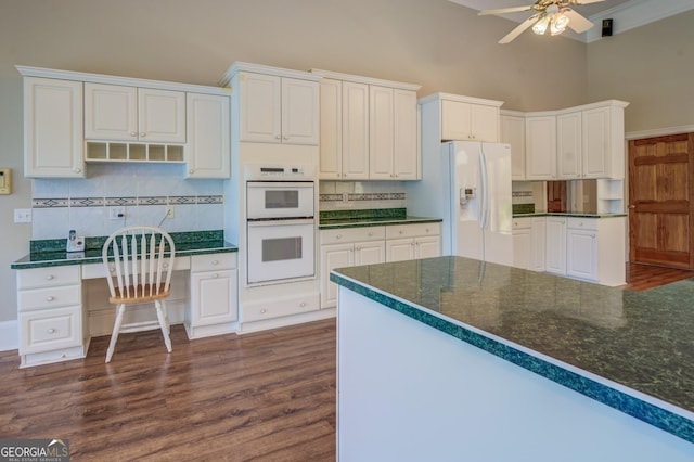 kitchen featuring tasteful backsplash, white appliances, dark wood-type flooring, built in desk, and white cabinetry