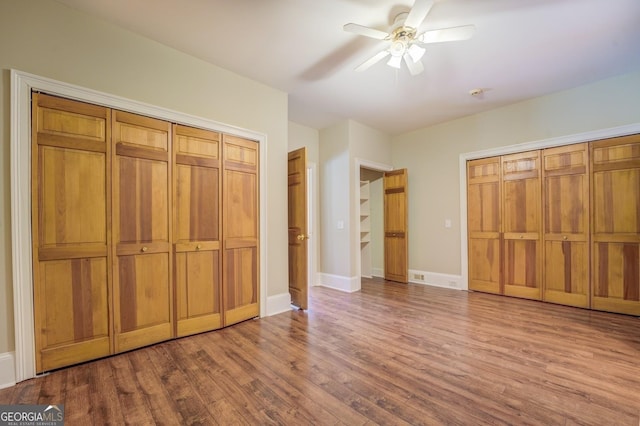 unfurnished bedroom with ceiling fan, wood-type flooring, and two closets