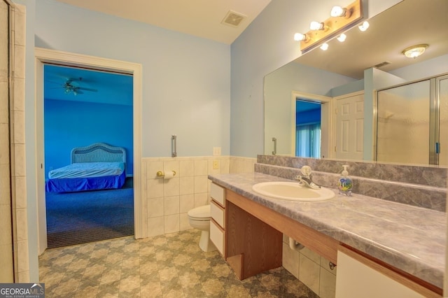 bathroom featuring ceiling fan, sink, toilet, a shower with shower door, and tile walls